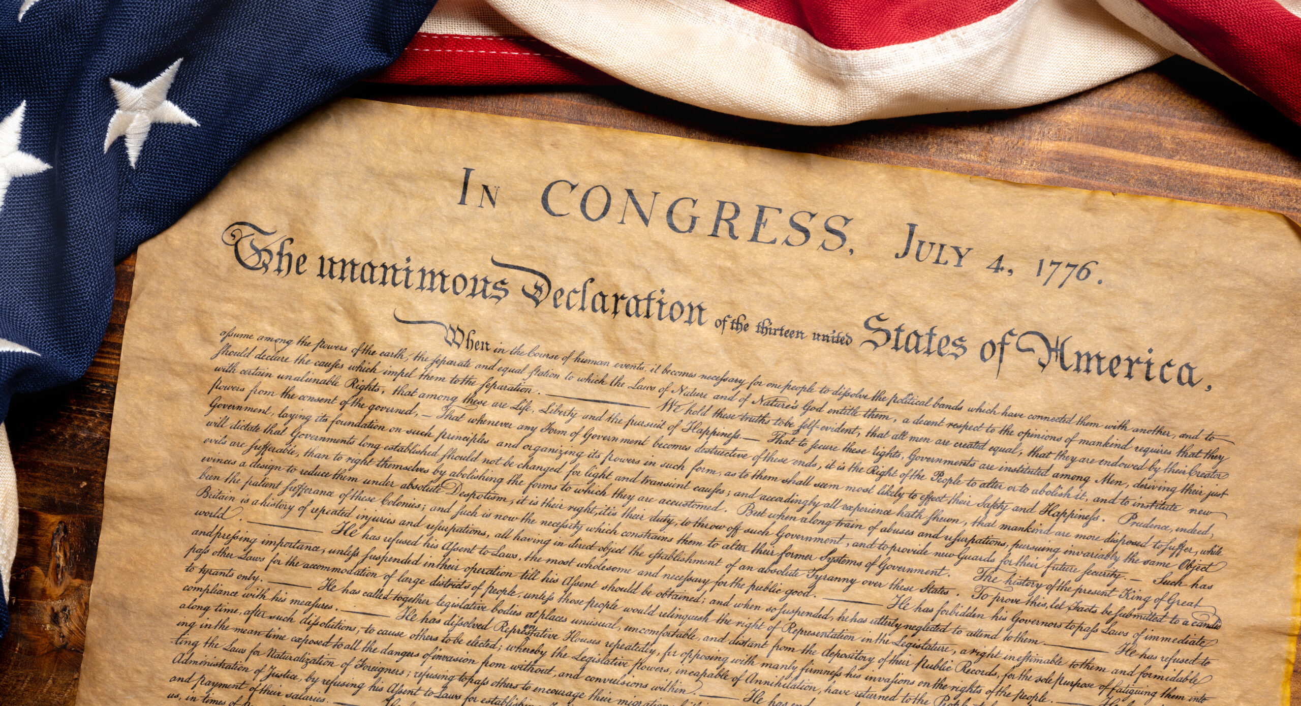 A copy of the United States Declaration of Independence with a vintage American flag on a wood background