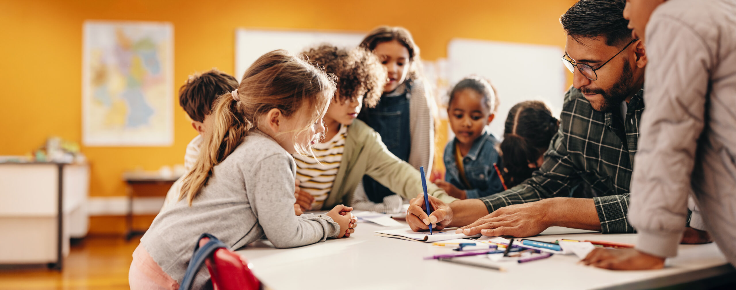 Teacher shows his students how to draw using a coloring pencil in a classroom